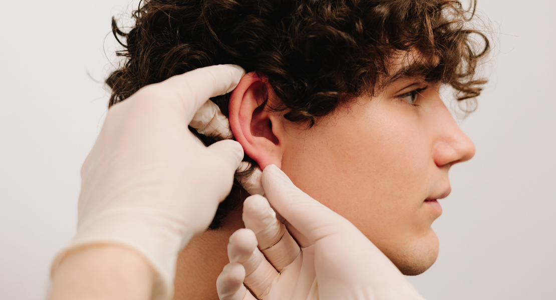 Chirurg w rękawiczkach bada ucho pacjenta przed zabiegiem otoplastyki.